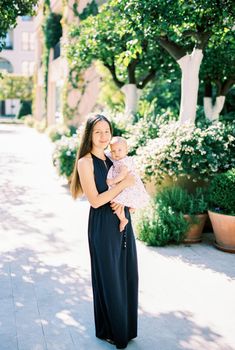 Mom with a baby in her arms stands near flower pots on the street. High quality photo