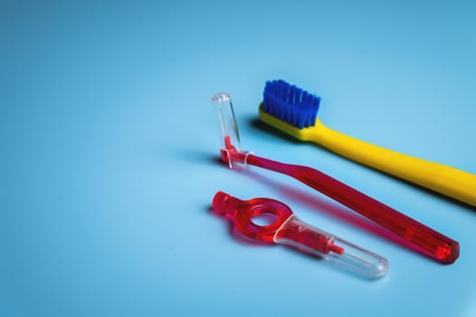 bright colored toothbrush with interdental orthodontic brush on blue background with copy space, close up. Oral hygiene concept.