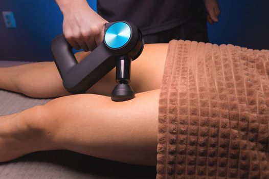 Close-up percussion thigh massage with a special electric device.