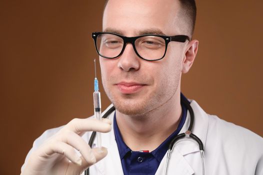 Handsome man in doctor uniform holding a syringe smiling happily, portrait studio shot.