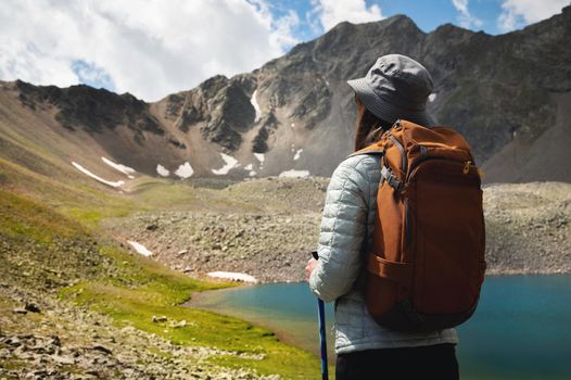 rear view, young woman enjoying mountain lake, tourist looks into distance at rocky peaks of mountain, summer vacation concept.