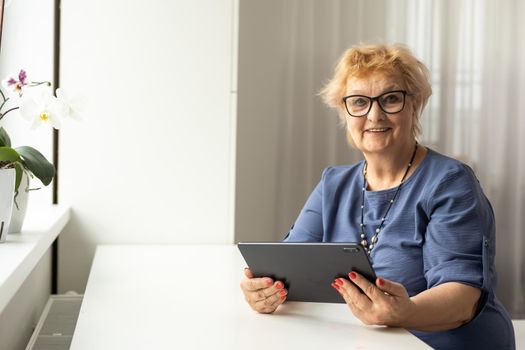 Authentic shot of a happy grandmother is making a video call to relatives with a laptop at home. Concept of technology, modern generation,family, connection, authenticity.