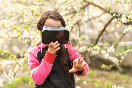 Full body little girl excited and entertained, playing with virtual reality glasses, exploring a fantasy world, trying to touch something