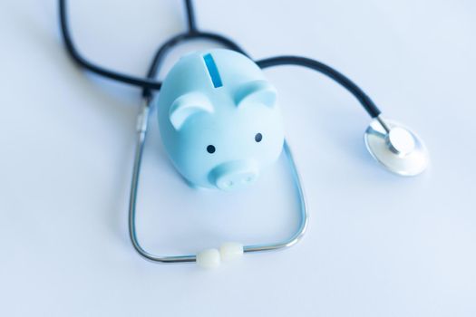 Piggy bank with stethoscope isolated on light blue background with copy space. Health care financial checkup or saving for medical insurance costs concept.