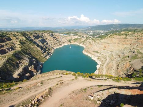 Flight over the turquoise surface of the lake in the center of the quarry. Industrial of opencast mining quarry with flooded bottom. Small lake in the shape of a heart