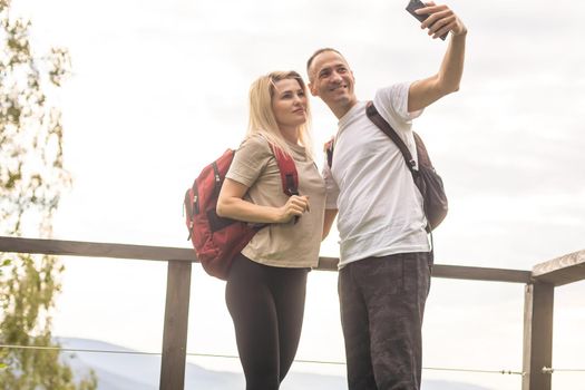 A man and a woman in tourist equipment are standing on a rock and admiring the panoramic view. A couple in love on a rock admires the beautiful views. A couple in love is traveling. A couple on a hike