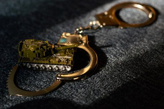 toy tank and handcuffs on a dark background.