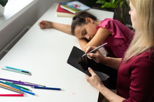 Professional female child psychologist working with a little preschool girl in a bright office. Woman makes notes about the condition of the girl on paper. Children's mental therapy