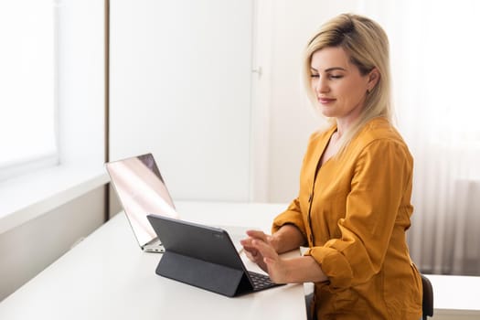 Young charming smiling caucasian sitting in living room, holding tablet and looking away