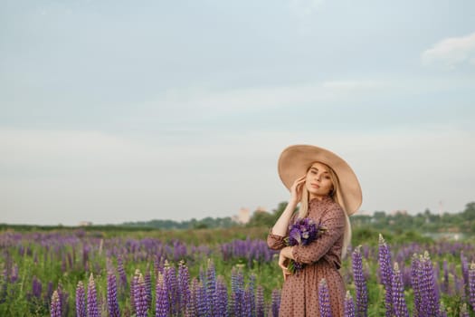 A beautiful woman in a straw hat walks in a field with purple flowers. A walk in nature in the lupin field.