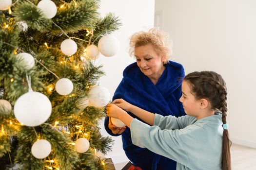 winter holidays and family concept - happy grandmother and baby granddaughter near christmas tree at home.