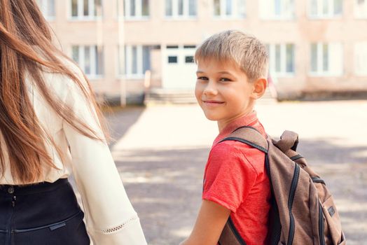 Happy elementary school learner going to school with his mother, looking back to the camera