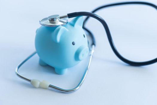 Piggy bank with stethoscope isolated on light blue background with copy space. Health care financial checkup or saving for medical insurance costs concept.