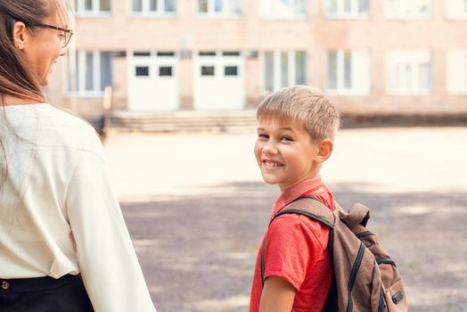 Pupil carrying backpack, holding parent's hand and looking back to the camera