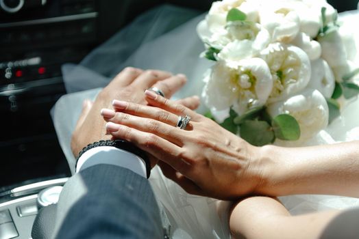 Newlyweds holding hands, holding hands in foreground, close-up of young couple's hands with wedding rings on ring fingers.