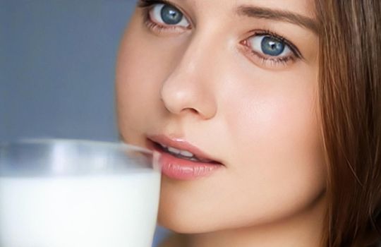 Happy young woman with glass of milk or protein milk shake, healthy cocktail drink for diet and wellness concept