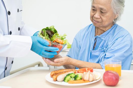 Asian senior or elderly old lady woman patient eating breakfast and vegetable healthy food with hope and happy while sitting and hungry on bed in hospital.