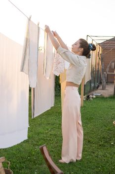 Laundry day. A woman hangs linen and towels on a tree in the courtyard of a village house. Summer cottage concept.