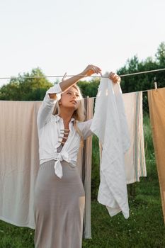 Laundry day. A woman hangs linen and towels on a tree in the courtyard of a village house. Summer cottage concept.