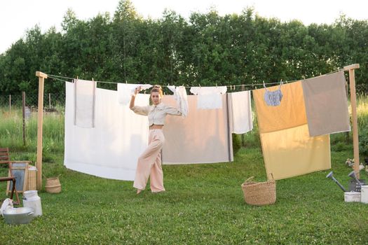 Laundry day. A woman hangs linen and towels on a tree in the courtyard of a village house. Summer cottage concept.