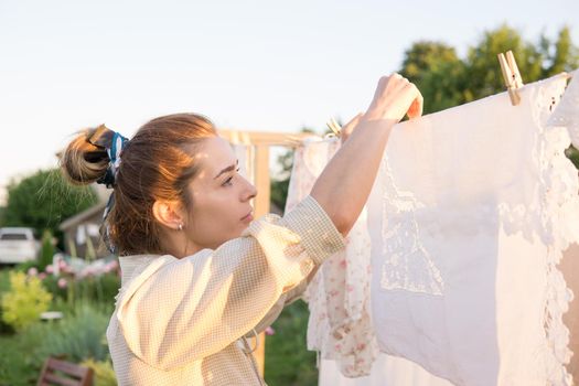 Laundry day. A woman hangs linen and towels on a tree in the courtyard of a village house. Summer cottage concept.