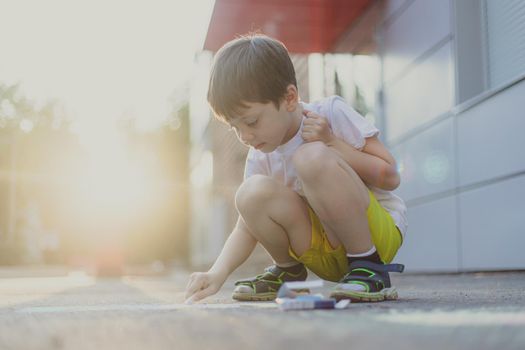 A boy draws a lifestyle with crayons on the asphalt . Children's classes. Children's drawings. Child psychology. Advertising of children's products