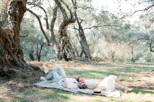 Man and woman lie head to head on a blanket in an olive grove. High quality photo