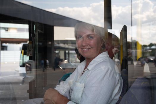 middle-aged caucasian woman sitting in bus pictures through glass with reflection of bus stop and public transport. High quality photo