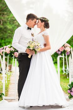 Wedding couple under the flower arch at the wedding ceremony outdoors in the park