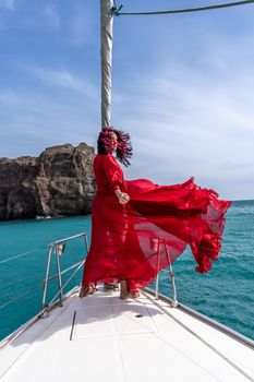 Attractive middle-aged woman in a red dress on a yacht on a summer day. Luxury summer adventure, outdoor activities