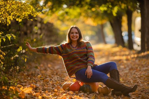 Smile woman sitting on the pumpkin on the autumanl maple leaves. Cozy autumn vibes Halloween, Thanksgiving day.