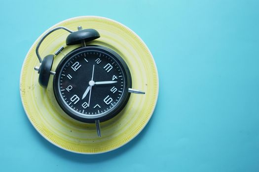 Alarm clock on plate on wooden table, top view