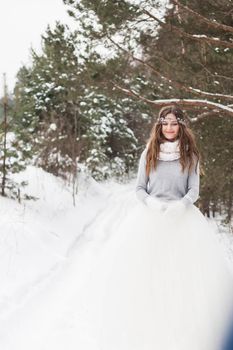 Beautiful bride in a white dress with a bouquet in a snow-covered winter forest. Portrait of the bride in nature.