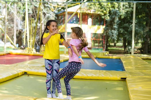 Little pretty girls having fun outdoor. Jumping on trampoline in children zone. Amusement park.