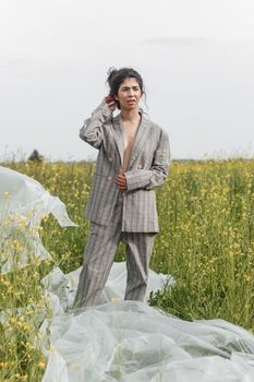 An Asian model poses in a field of yellow flowers for a clothing brand, polyethylene is the main props for a photo shoot. The concept of manufacturing clothing from recycled plastic. A woman in a pantsuit is standing on a plastic bag.