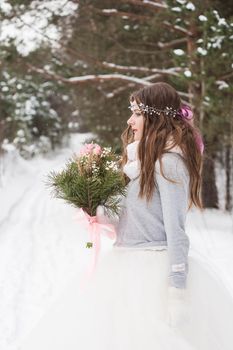 Beautiful bride in a white dress with a bouquet in a snow-covered winter forest. Portrait of the bride in nature.