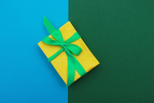 Yellow paper box with green ribbon on double background of blue and green. . Holiday concept. Christmas gift.