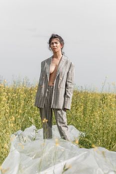 An Asian model poses in a field of yellow flowers for a clothing brand, polyethylene is the main props for a photo shoot. The concept of manufacturing clothing from recycled plastic. A woman in a pantsuit is standing on a plastic bag.