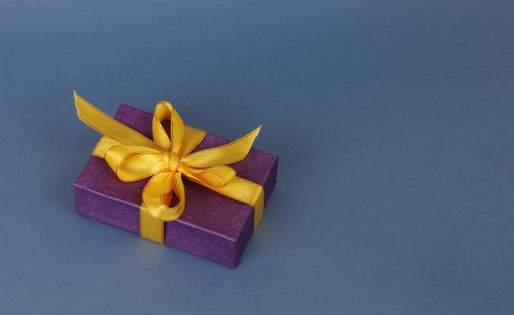 Dark blue paper box with yellow ribbon and bow on a light blue paper background.