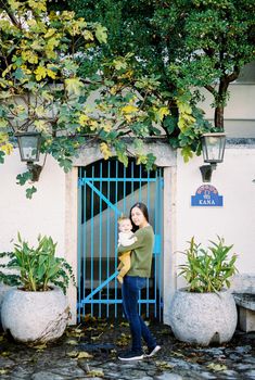 Mom with a baby in her arms stands near a forged gate in a stone fence. High quality photo