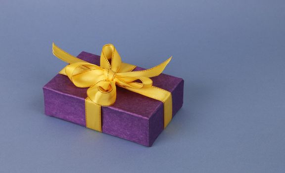 Dark blue paper box with yellow ribbon and bow on a light blue paper background. A festive concert. A gift box with a beautiful bow.