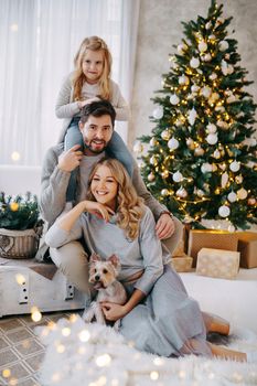 Happy family: mom, dad and pet. Family in a bright New Year's interior with a Christmas tree.