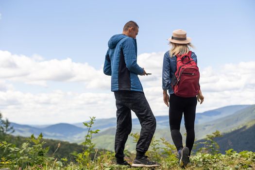 Rear view of hiking couple with backpack standing together on hill top enjoying beautiful landscape. Man and woman outdoors on hiking standing on a rock.