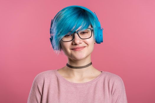 Pretty young girl with turquoise hair having fun, smiling, dancing with blue headphones in studio on colorful background. Music, dance, radio concept