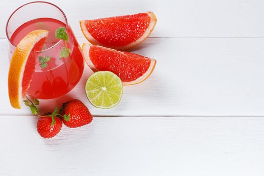 Fresh grapefruit juice in a glass with grapefruit slices, lime and mint on a wooden background. Copy space, selective focus