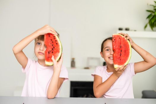Funny little sisters eating fresh juicy watermelon at home.