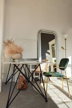 Comfortable velour chairs placed at table decorated with vases in classy styled room with mirror and lamp in sunlight