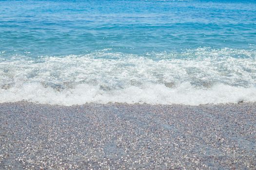 Pebble beach with azure sea water texture background