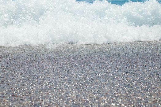 Pebble beach with azure sea water texture background