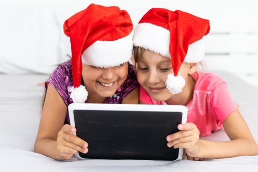 christmas, x-mas, winter, happiness concept - two adorable curly girls playing with tablet pc.